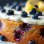 Close-up of a lemon blueberry mascarpone cake with fresh blueberries and lemon slices on top, showing the layers and textures.