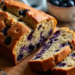 Sliced blueberry lentil bread loaf on a wooden cutting board with fresh blueberries.